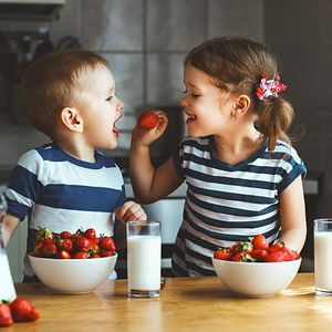 Image of two kids eating strawberries and milk. 