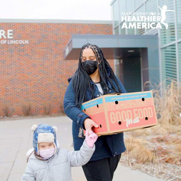 Perla from Lincoln, NE and her daughter walking with a Good Food for All produce box