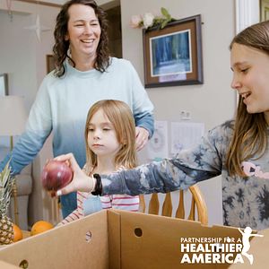 Joanna looking at a Good Food for All box with her family 