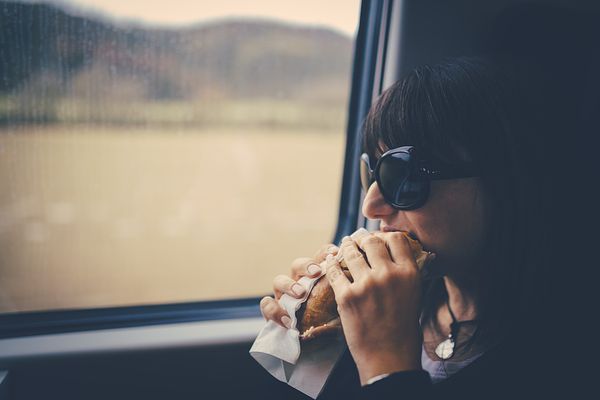 Woman eating a sandwich and staring out a train window.