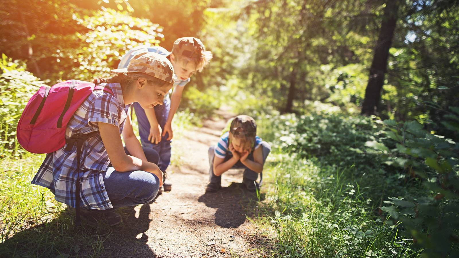Young hikers stop to observe an object on the ground during a hike.