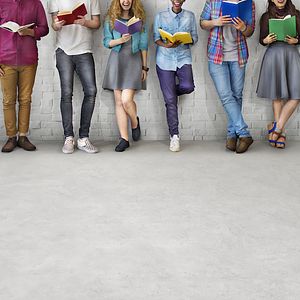 Image of college students leaning against a wall holding books. 