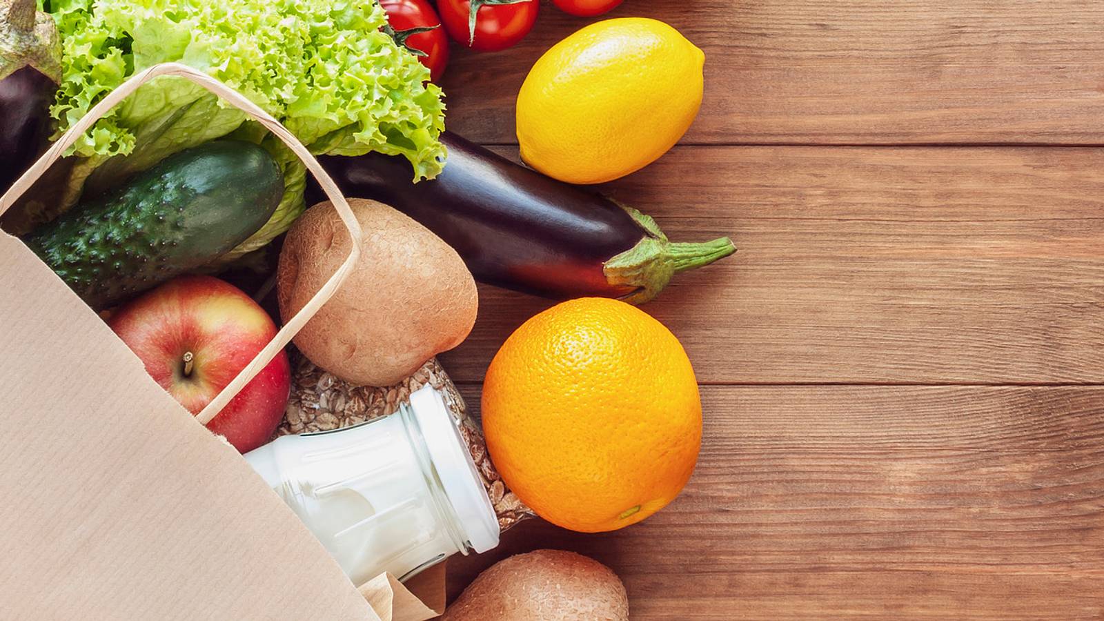 Bag of groceries with fruits and vegetables, spilling out onto a wooden table.