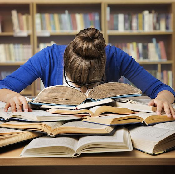 Image of a stressed college student with their head down on a large pile of textbooks. 