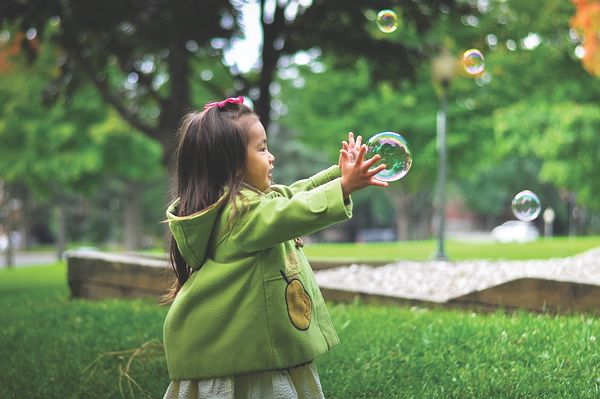 Image of a girl in a rain coat popping bubbles outdoors. 