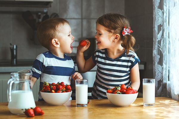 Image of two kids eating strawberries and milk. 