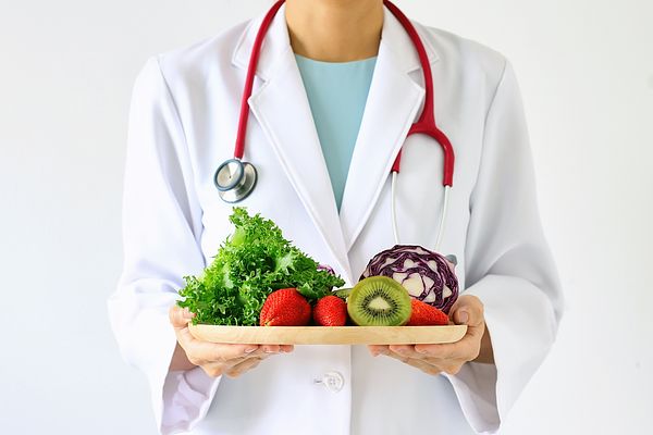 Image of a doctor in a lab coat holding a tray of fruits and vegetables.