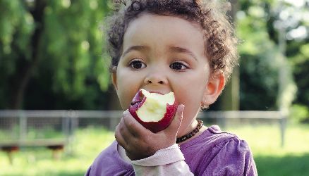 Image of young child eating an apple in Partnership for a Healthier America's 2016 Annual Progress Report. 