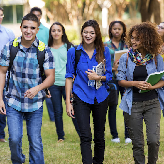 Image of diverse group of college students walking across a campus. 