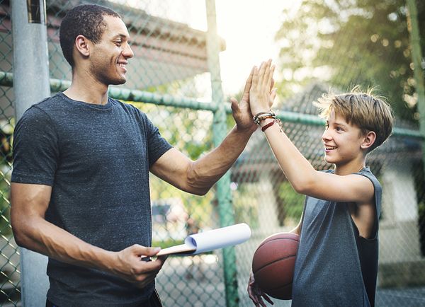 Image of a man and young boy giving one another a high five after playing basketball. 