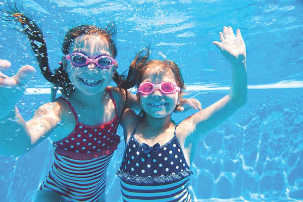 Image of two young girls swimming and posing in a pool. 