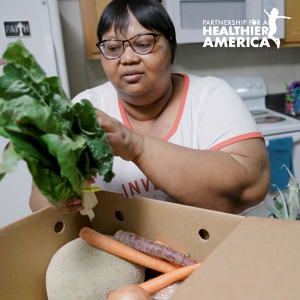 Charmaine from Good Food for All in New Orleans, LA looking at a produce box filled with fresh fruits and vegetables.
