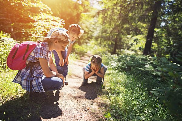 Young hikers stop to observe an object on the ground during a hike.