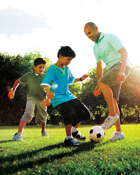 Image of a man and two young boys playing soccer in a field. 