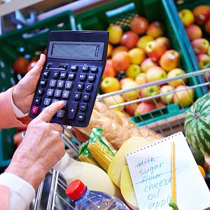 Image of a person holding a calculator in front of produce at the grocery store. 