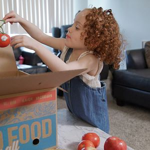 girl pulling tomato from box