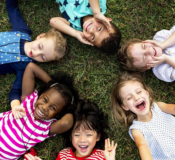 Group of diverse children laying in the grass looking up into the photographer's camera. 