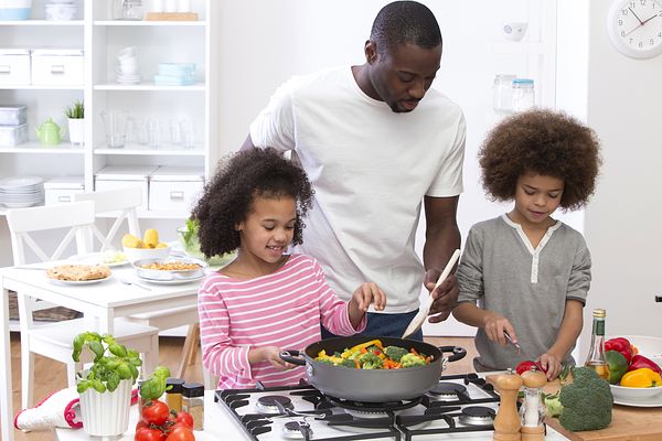 Photo of a father and two children cooking a meal together.